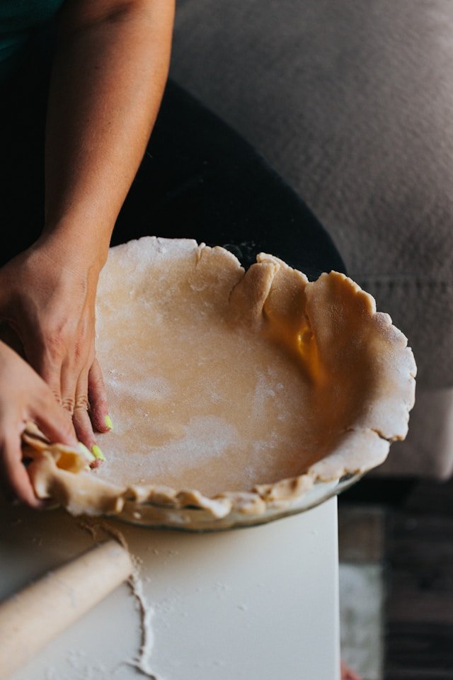 Hand molding pastry into a round pie plate. The Inspired Apron contact us page